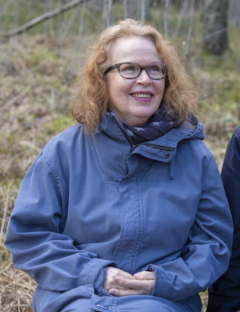 Riitta Jalonen sits in the forest and looks at the camera.