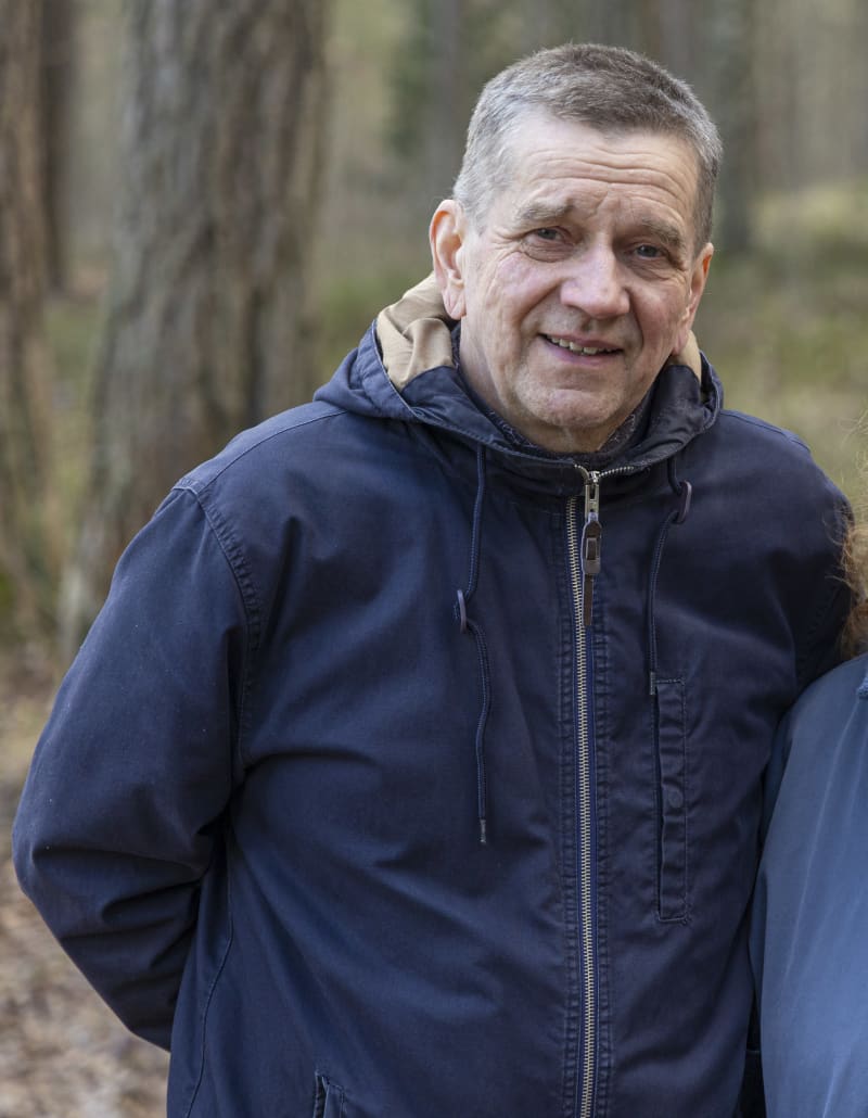 Olli Jalonen stands in the forest and looks at the camera.