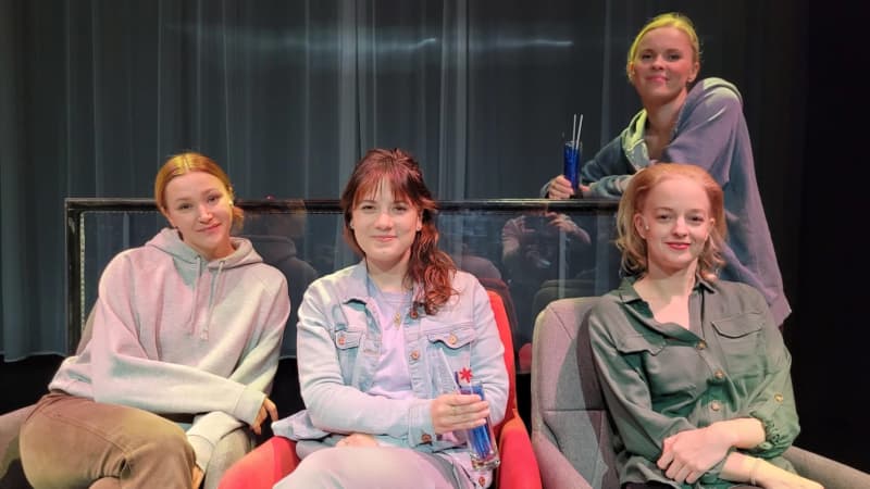 Four women sit on a theater stage during a rehearsal break