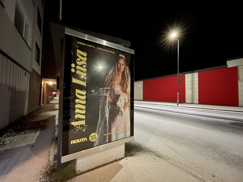Anna Liisa theater performance poster at the bus stop.  There is snow on the road.