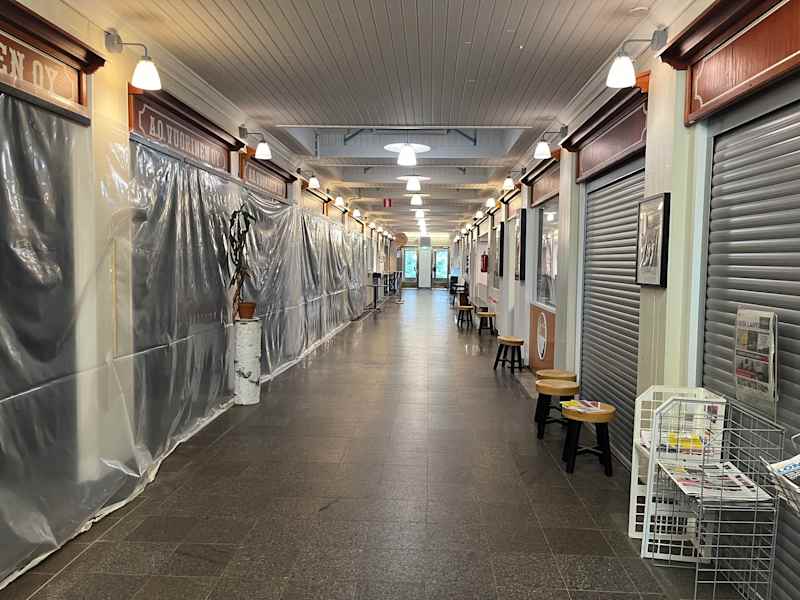 A hallway with door openings.  Some of the openings are covered with translucent plastic, some of the roller bales in front.  There are round stools in the hallway.