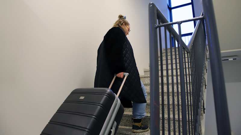 A woman walks up the stairs, dragging a suitcase behind her.