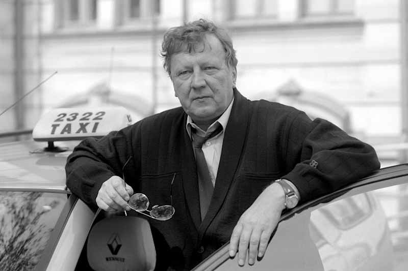 A black and white picture where Sulevi Peltola leans on a taxi and holds sunglasses in his hand.