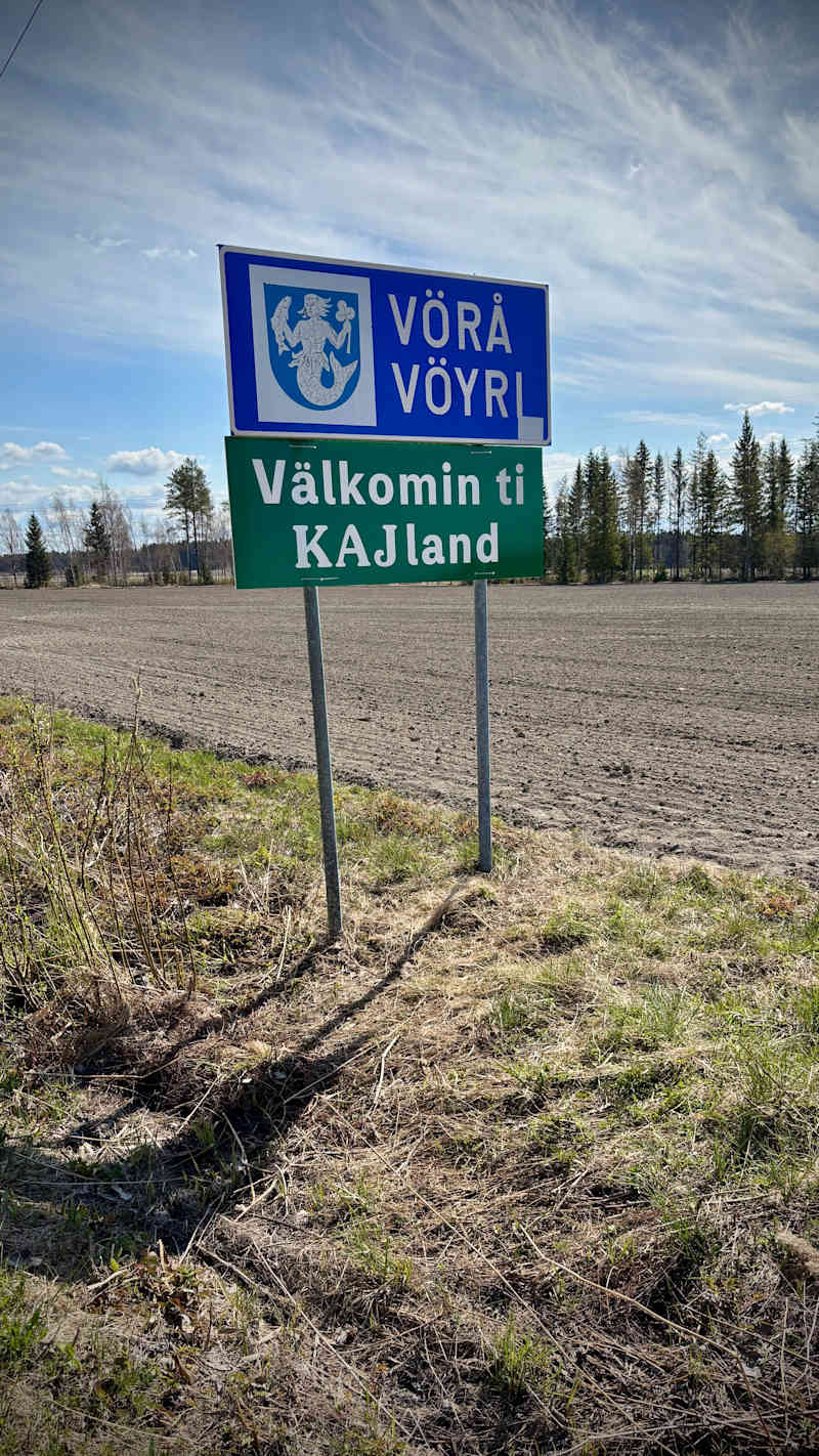 The road sign is on the roadside at the edge of the field.