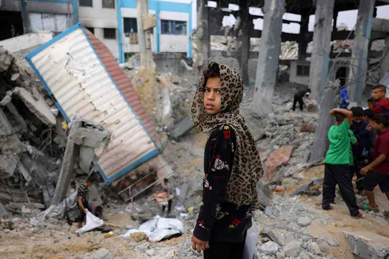 A Palestinian girl looks at the camera in the middle of the school ruins.