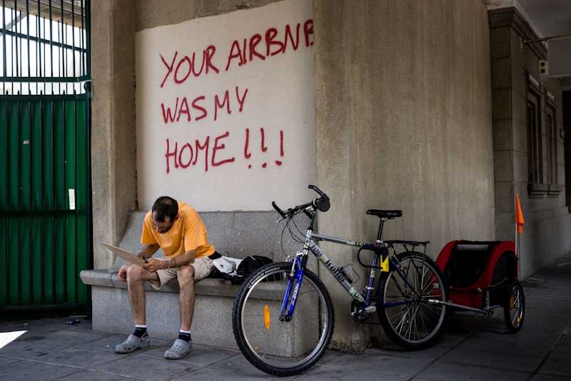 The man is sitting in the doorway.  Above him is spray painted: \
