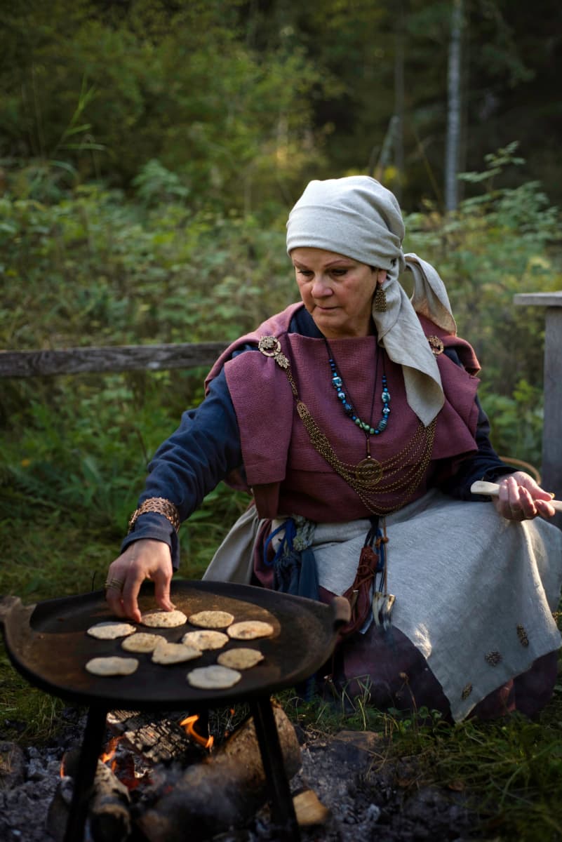 Nainen rautakautisissa vaatteissa paistaa leipää. 
