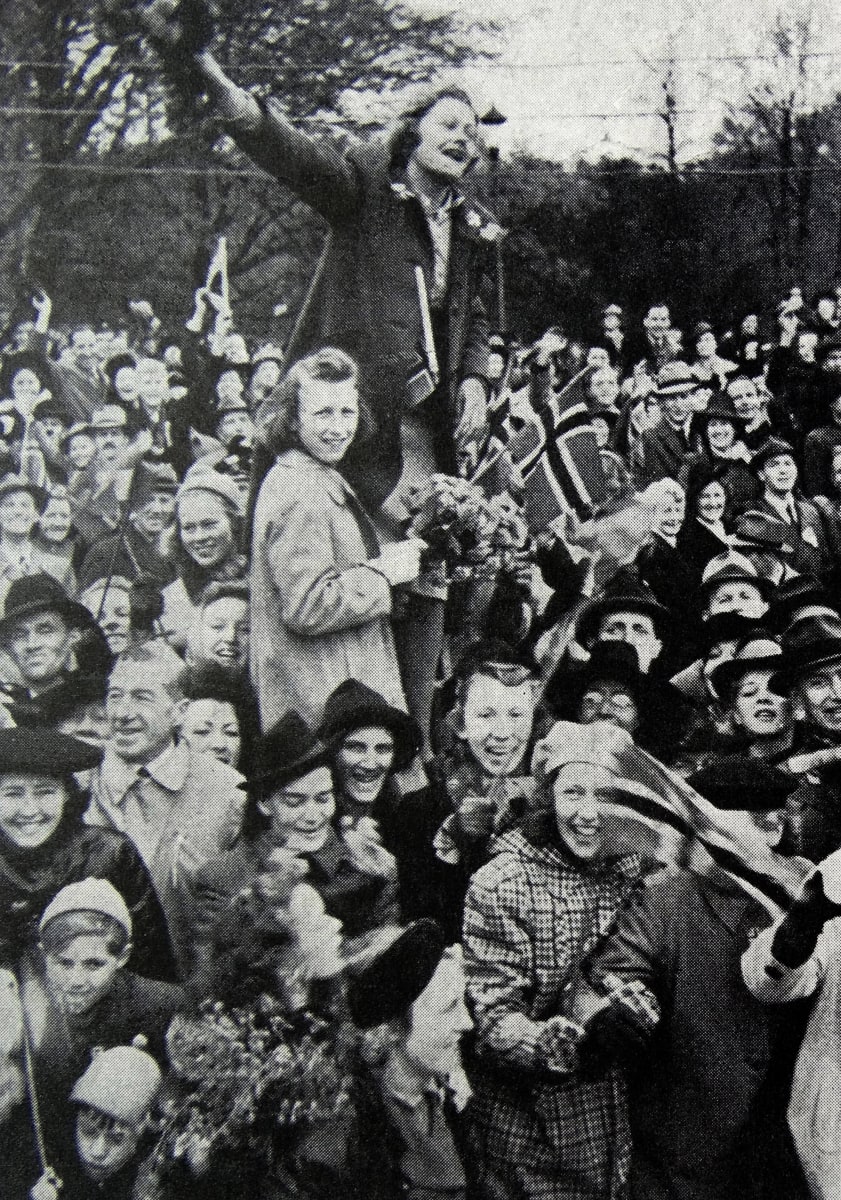 Nainen ja tyttö seisovat korokkeella ihmisjoukossa, tytöllä kädessä Norjan lippu.