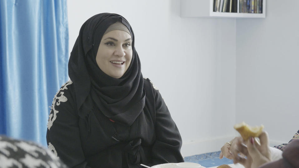 Afrah Al Bayaty istuu sängyllä pukeutuneena mustaan hijabiin ja hymyilee.