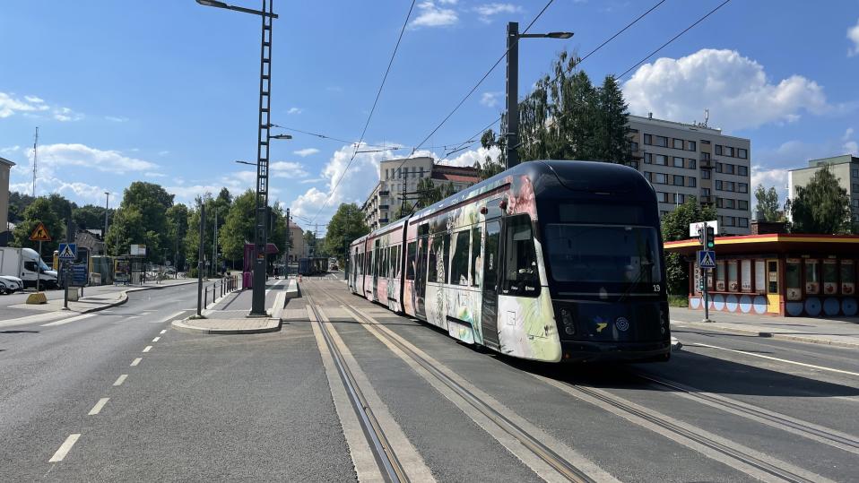 Tampereen ratikka kuvattuna edestäpäin. Aurinko paistaa, ja taivas on sininen.