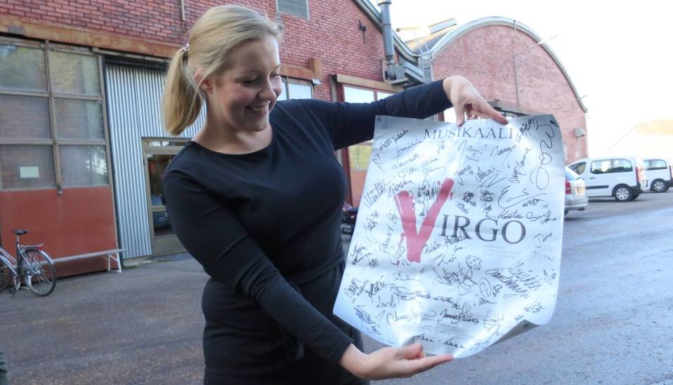 Laura Valkiala esittelee nimikirjoituksilla koristeltua Virgo-musikaalin julistetta