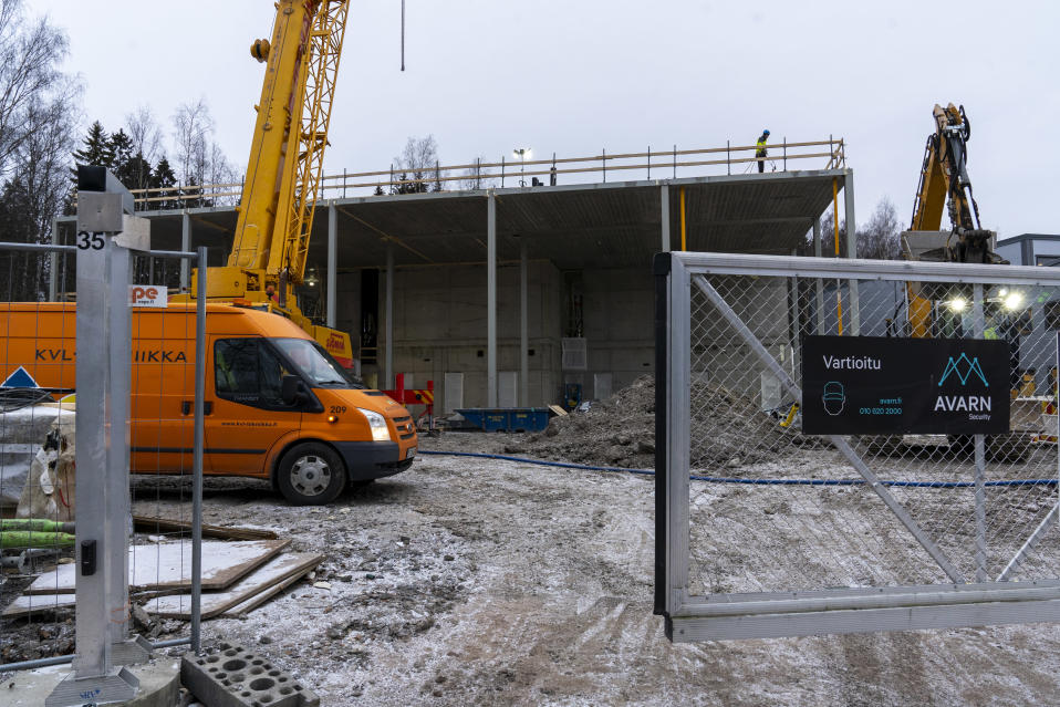 Konalaan valmistuvan Helsingin pelastuslaitoksen työmaa, talon runko pystyssä, etualalla työmaan portti, pakettiauto, nosturi ja kaivuri taustalla.