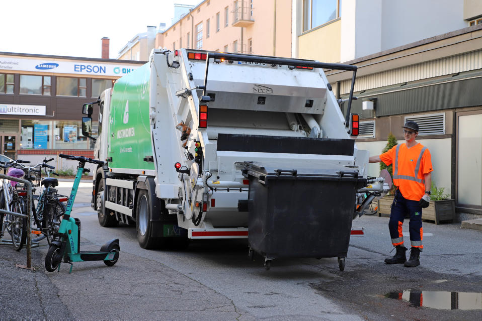 Jäteautonkuljettaja Tuure Vanhanen tyhjentää roskalaatikkoa jäteautoon Jyväskylässä, sähköpotkulauta auton vieressä.