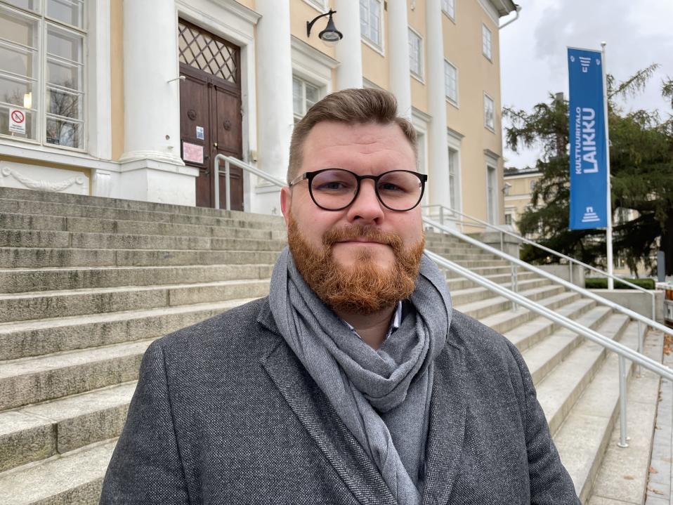  Taidetestaajat-toiminnan päällikkö Joonas Keskinen hymyilee varovaisesti Tampereen vanhan pääkirjaston rappusten edessä.