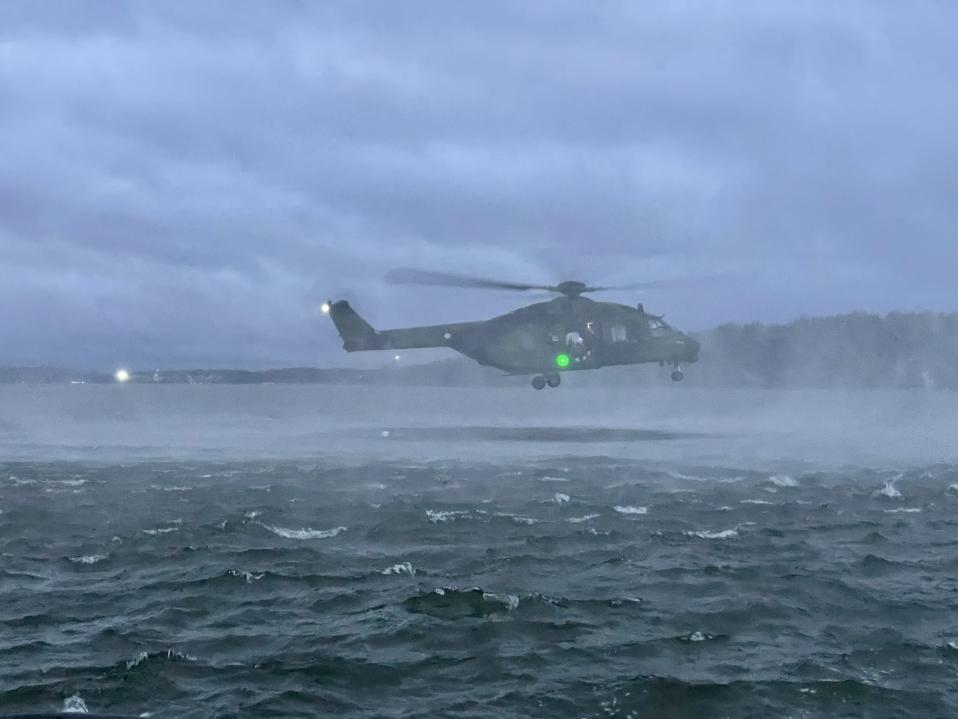 NH-90 kuljetuskopteri leijailee matalalla järven yläpuolella.