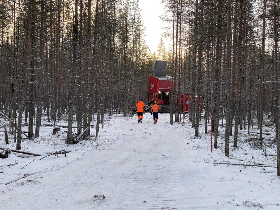 Kairauskone metsässä, miehet oransseissa puvuissa kävelevät koneelle päin. 