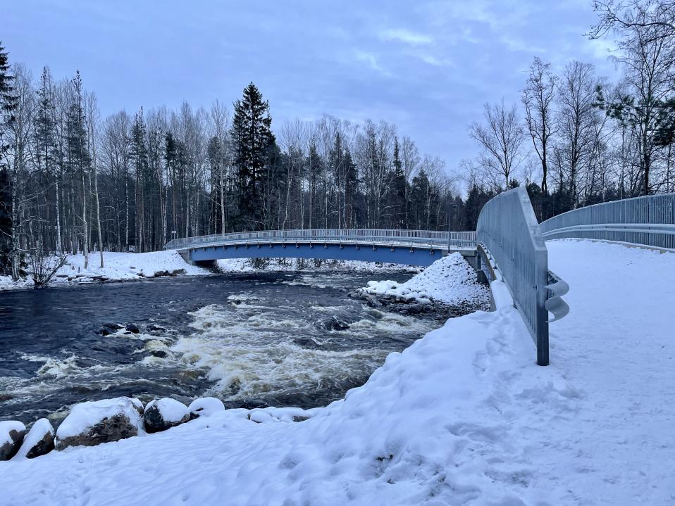 Sininen silta kaareutuu vasemmalle kosken yli.