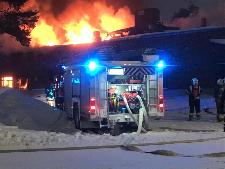 Pelastuslaitoksen ajoneuvo on parkkeerattu palavan rakennuksen eteen. 