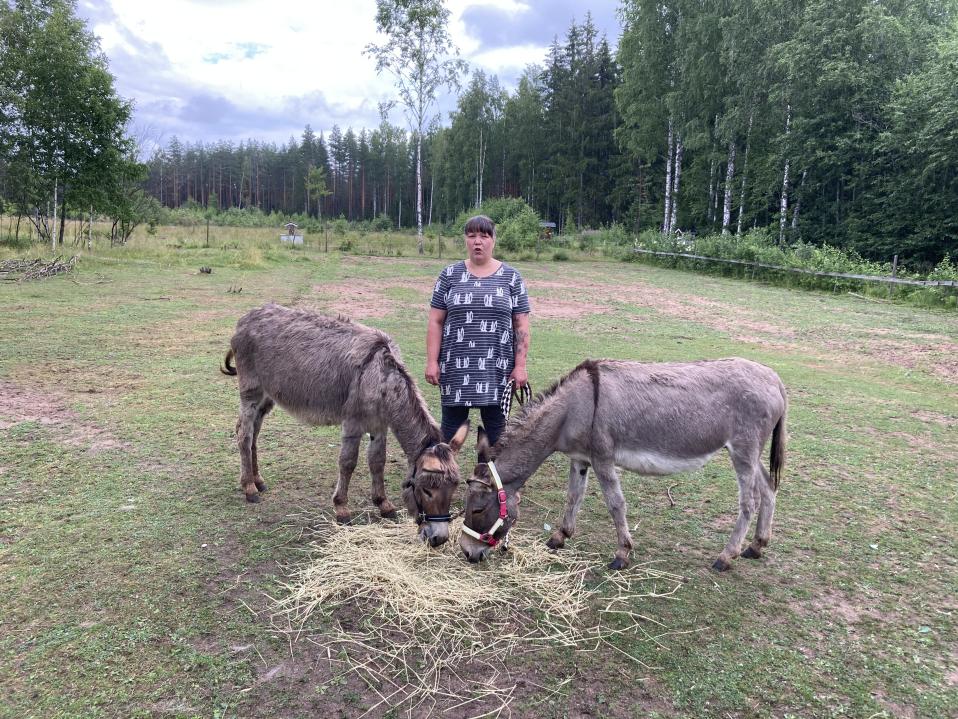 Nainen ja kaksi aasia kesäisellä nurmikolla.