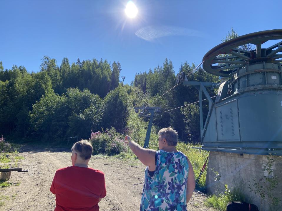 Juupavaaran camping-alueen aniharvoihin camping-kausipaikkalaisiin lukeutuva naiskaksikko seisoo selin kameraan rinnehissin pyörän vieressä. Toinen osoittaa kädellä ylös Venäläisvuoreen päin.