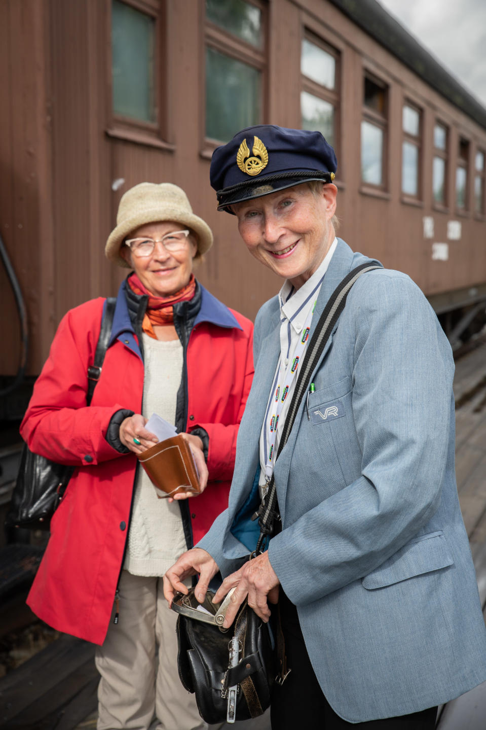 Kirsi Parviainen myy konduktööripuvussa matkalippuja Ulla Martinille vanhan junanvaunun vieressä.