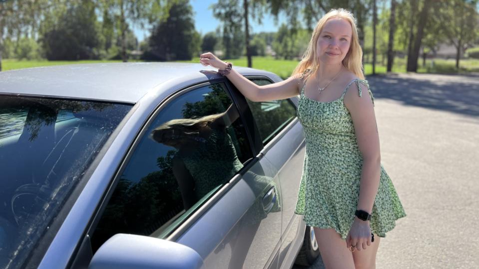 Minimekkoon pukeutunut Mirva Virtanen poseeraa siniharmaan Audinsa vieressä. 