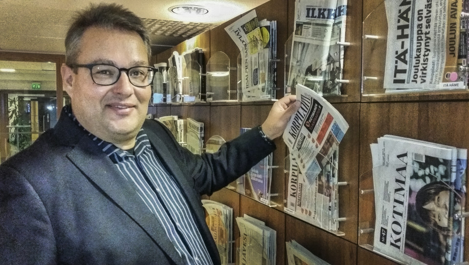 Mies esittelee paikallislehteä lehtihyllystä