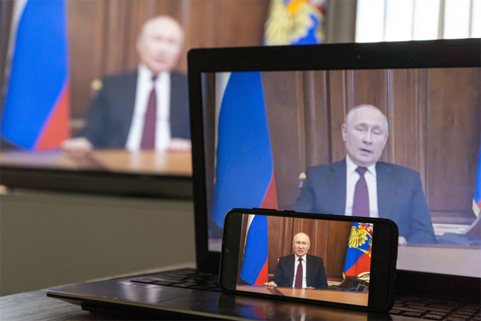 Puhelin, tietokonenäyttö ja tv-ruutu, joissa kaikissa puhuu Vladimir Putin kirjoituspöytänsä takaa, molemmilla puolilla Venäjän lippu