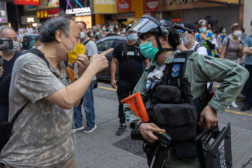 Mielenosoittaja osoittaa sormella poliisia, molemmilla kasvomaskit.