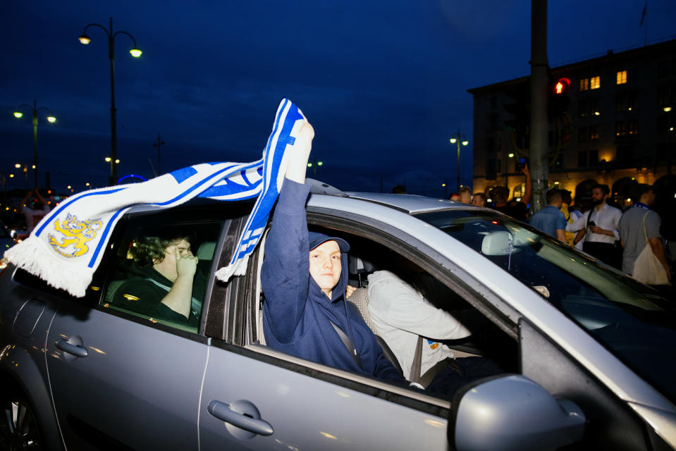 The owl fan sits in the car and the Finnish flag flies.