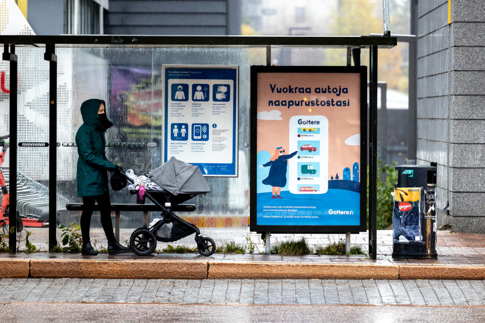 Nainen lastenvaunujen kanssa bussikatoksessa kasvomaskiin suojautuneena.