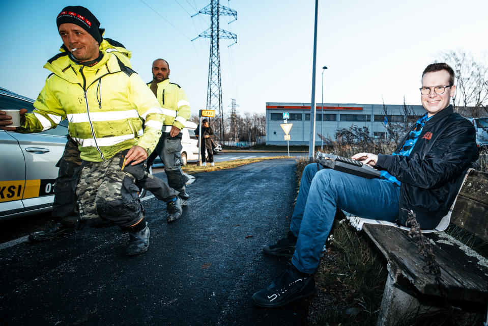 Janne Rinta istuu penkillä taksiasemalla ja työmiehiä ohittaa hänet.