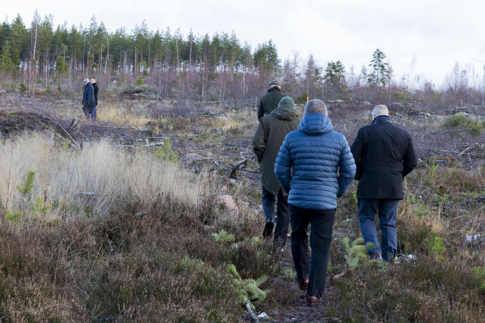 Kaupunginjohtajat sekä Cursorin ja Malmijalostuksen edustajat kävelevät Keltakalliolla tontilla, jolle tulee tehdas. Puutonta metsämaastoa, miehet kävelevät selin kameraan.