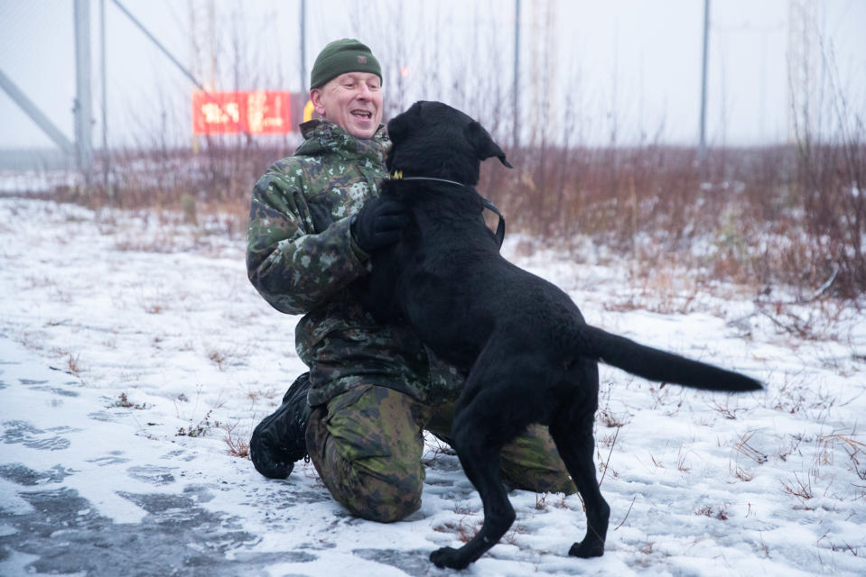 Mies ja musta labradorinnoutaja, miehellä maastopuku yllään ja hymyilee koiralle. 