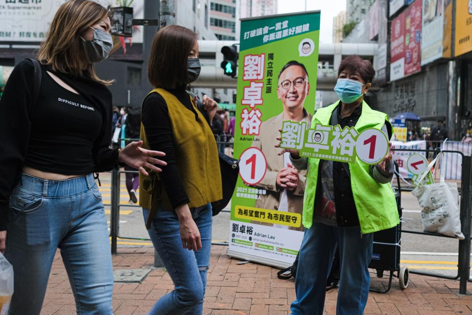 Jalankulkijat ohittavat vaalimainosta pitelevän naisen Hongkongissa.