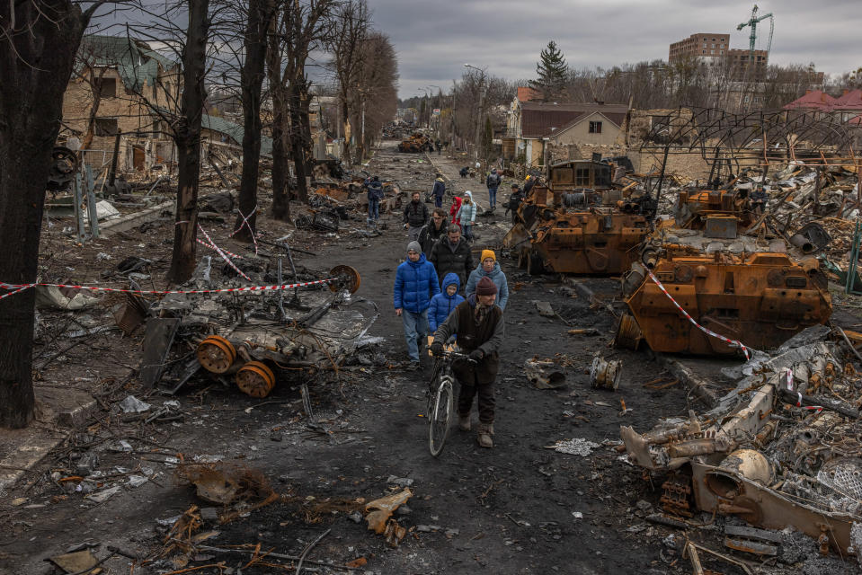 Ihmiset kävelevät kadulla tuhoutuneiden sotilas ajoneuvojen ja tuhoutuneiden rakennusten läpi.