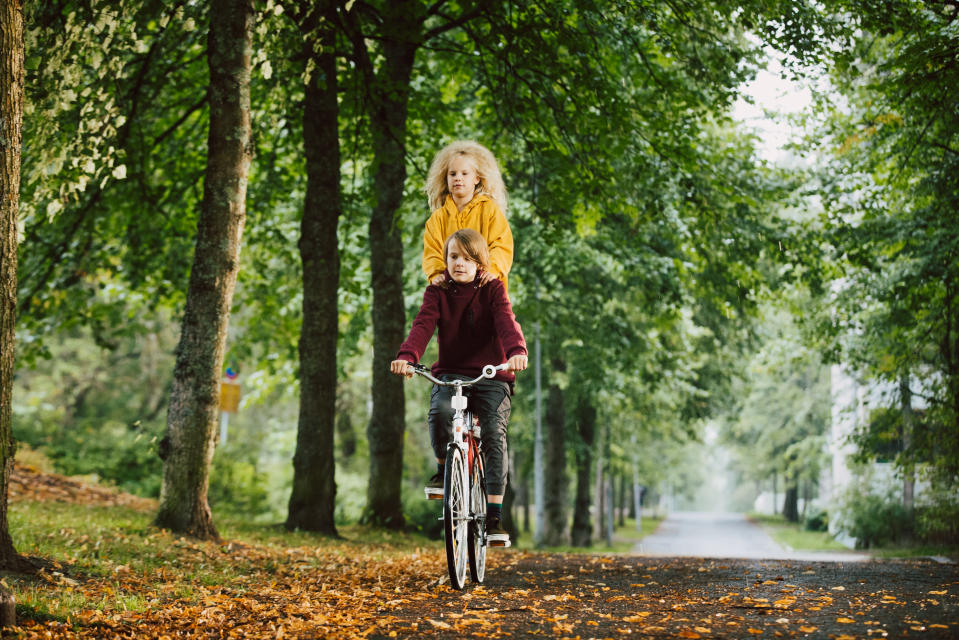 Lapsi ajaa polkupyörää metsätiellä, toinen lapsi seisoo kyydissä tarakalla.