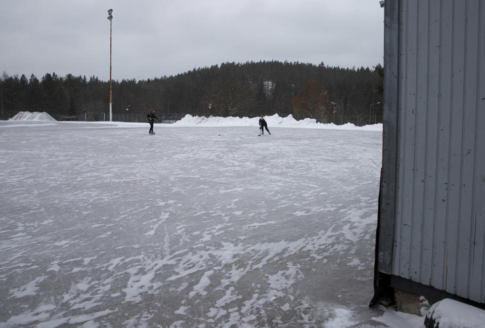 kaksi luistelijaa ulkojäällä, heillä on jääkiekkomailat kädessä.