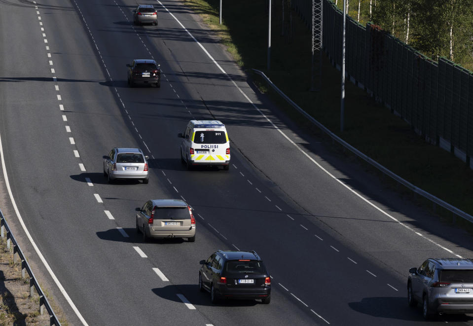 Henkilöautoja ja poliisiauto ajavat tiellä.