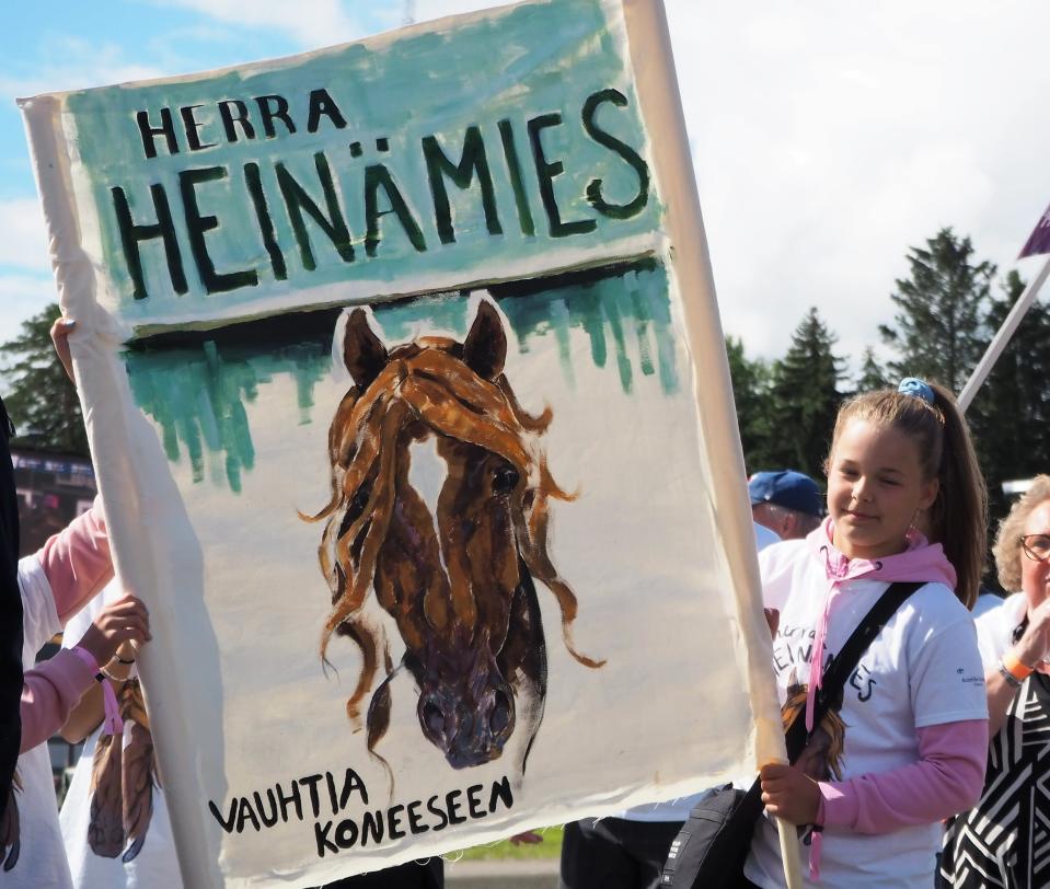 Lapsi pitelee banderollia, johon on maalattu Herra Heinämies -hevonen.