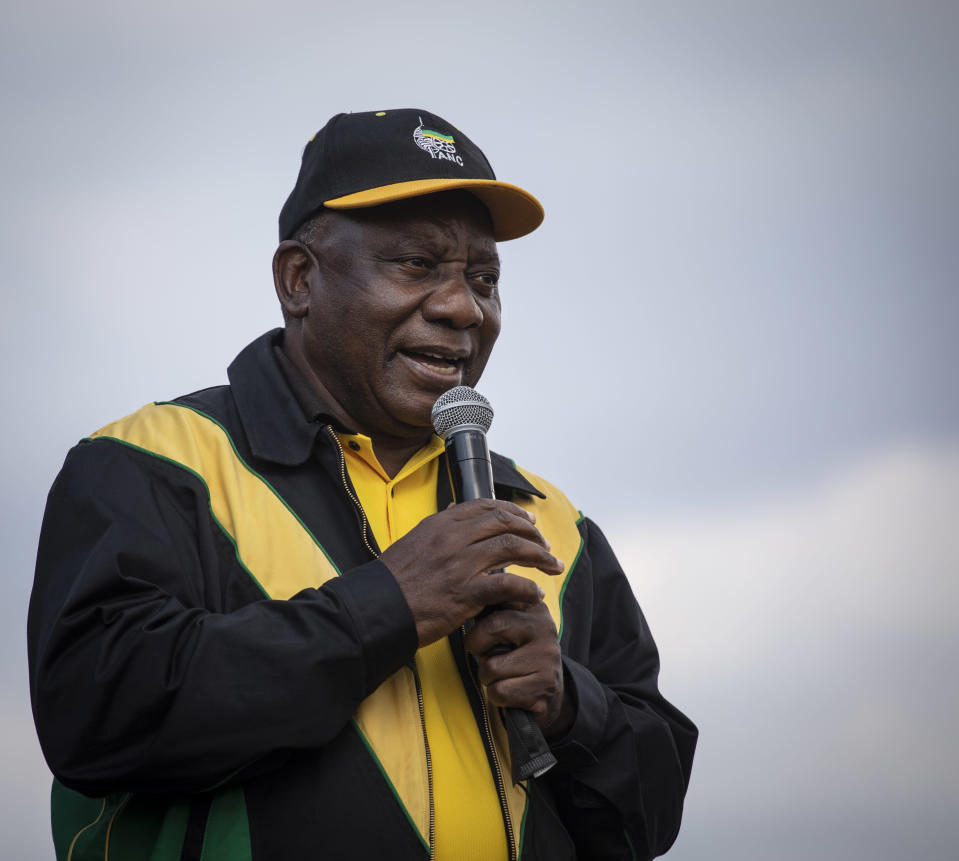 Cyril Ramaphosa puhuu mikrofoniin. Takki ja lippis yllään. 