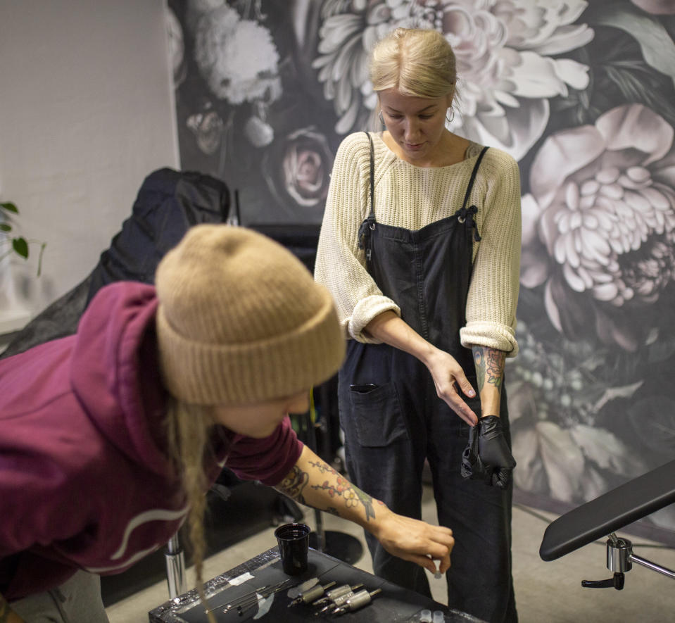 Tatuointiyrittäjä Leena Lumilampi ja hänen kollega The Flower Shop tatuointiliikkeestä asettelemassa värejä tatuointeha varten. Leena edessä pipo päässä.