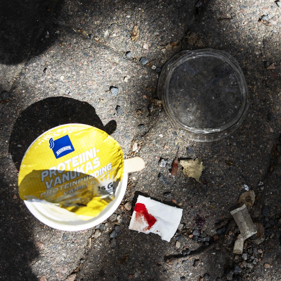 An empty can of protein pudding, a bloody bandage, a used needle and snuff lie on the pavement.