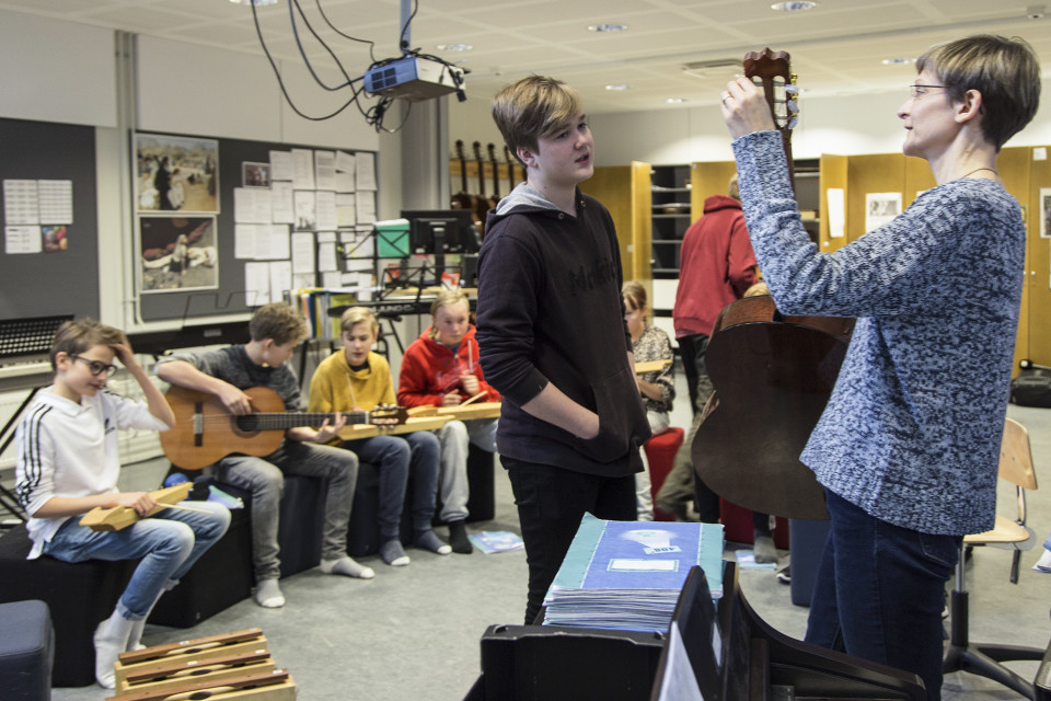 Opettaja virittelee akustista kitaraa ja juttelee oppilaan kanssa.