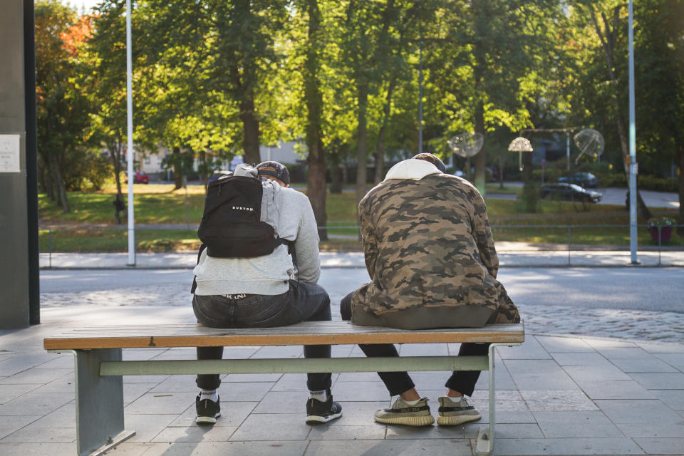 Kaksi nuorta miestä istuu puistonpenkillä selin kuvaajaan.