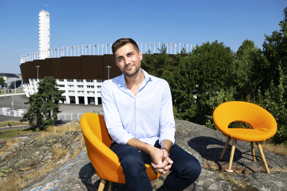 Mies istuu kalliolla oranssilla tuolilla, taustalla näkyy olympiastadion ja toinen oranssi tuoli.