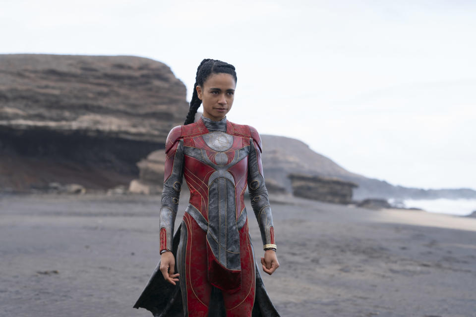 Eternals-elokuvan supersankari Makkari eli näyttelijä Lauren Ridloff punaisessa supersankariasussaan kivisellä rannalla.