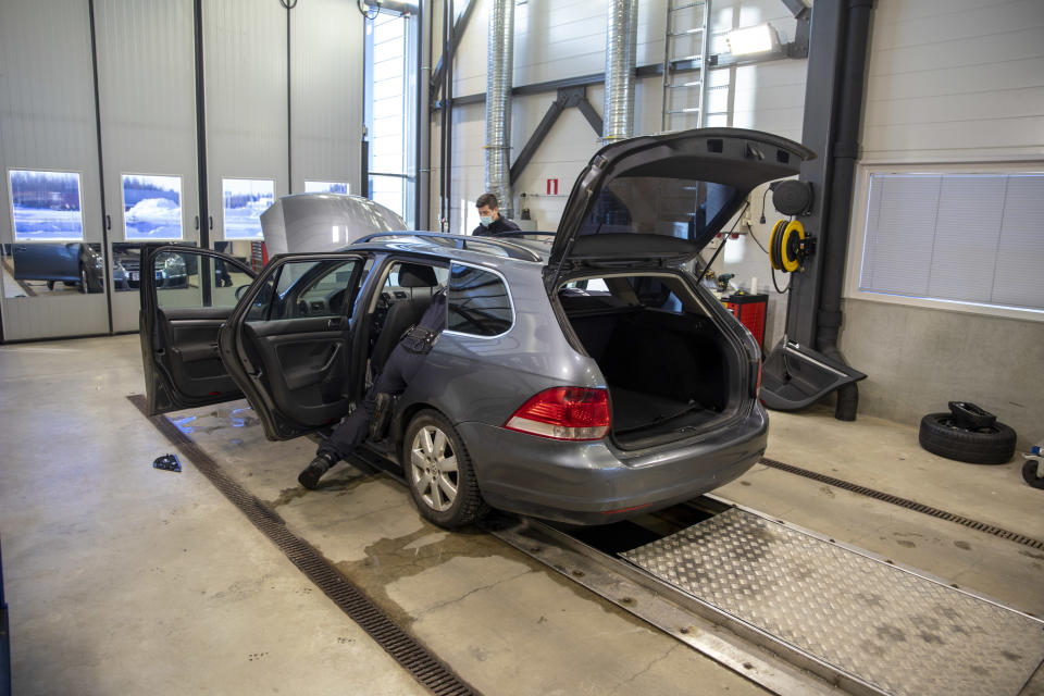 tullin työntekijät tarkastavat farmariautoa tarkastustallissa. Auton ovet ja takaluukku ovat auki.