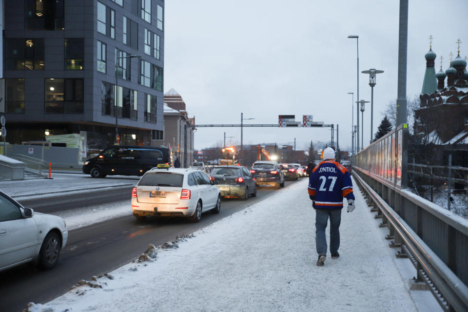 Tapparan paitaan pukeutunut ihminen kävelee jalkakäytävällä, vieressä autojono.