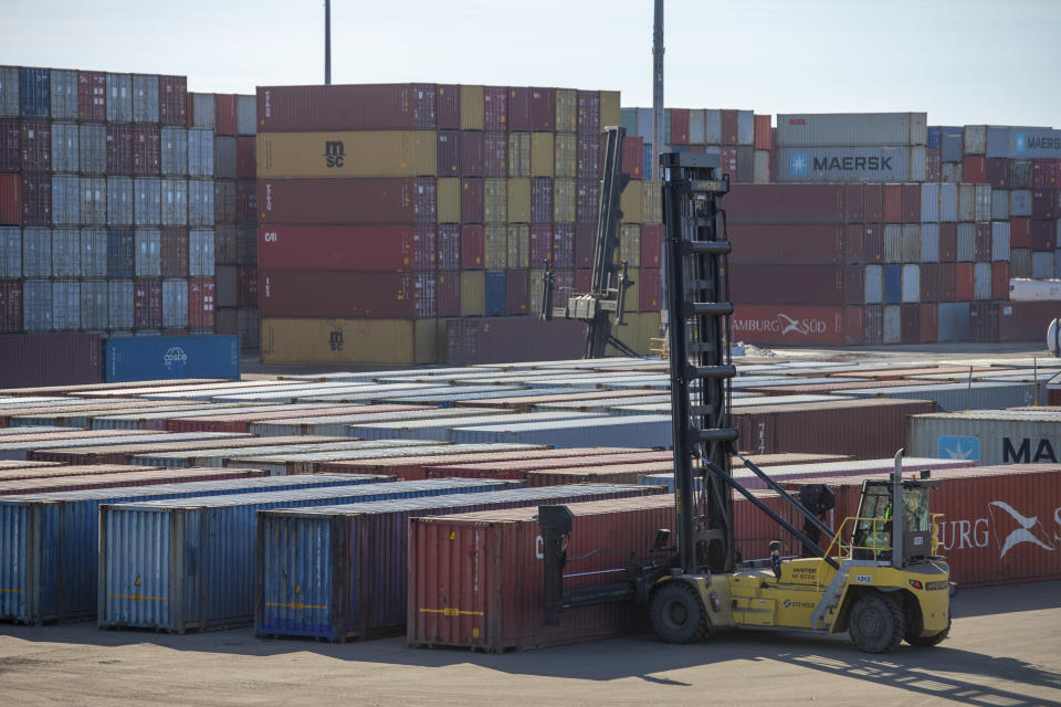 satamakentällä satoja kontteja riveissä ja pinoissa. Etualalla satamatrukki nostaa konttia ilmaan